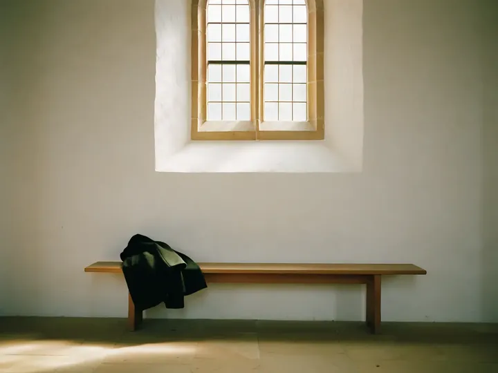 Holzbank in einem hellen Flur unter einem hohen Fenster, darauf eine abgelegte Jacke